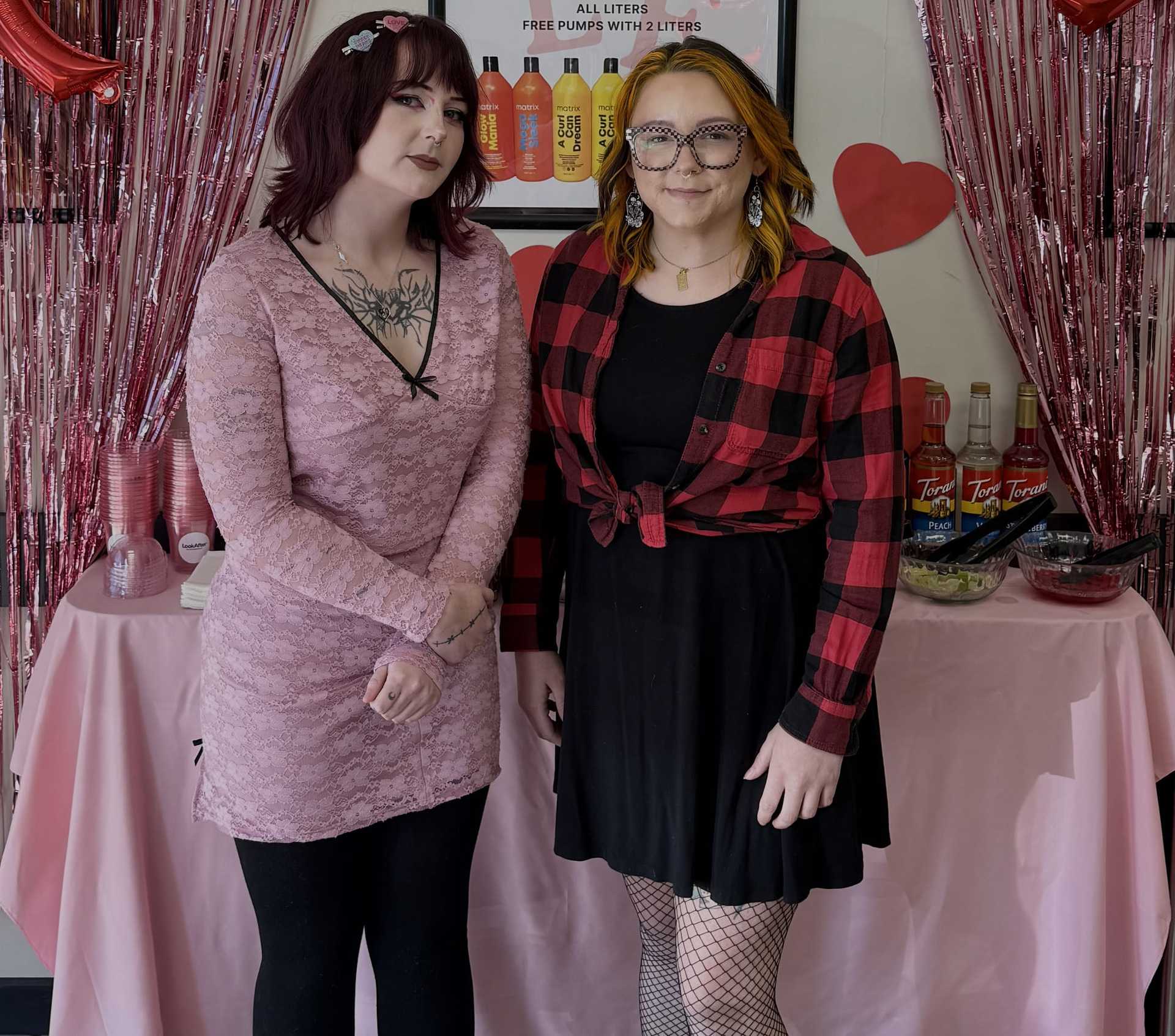 Two women standing in front of a decorated table with pink streamers and heart decorations.